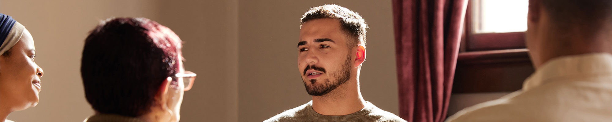 Un groupe de personnes assises en cercle lors d’une séance de discussion ou de thérapie, avec un homme au centre qui pose ses mains sur sa poitrine, exprimant une émotion ou une réflexion