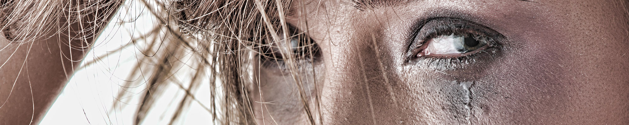Gros plan sur le visage d’une femme en pleurs, une larme coulant sur sa joue, les cheveux en partie collés à son visage et l’expression marquée par la détresse.